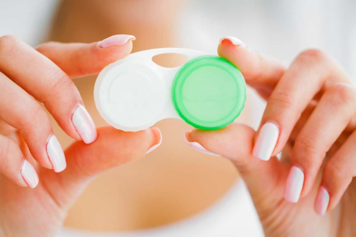 Osoba trzyma pojemnik do przechowywania soczewek, co jest ważne w kontekście pielęgnacji soczewek kontaktowych.