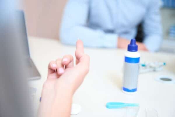 Osoba trzyma soczewkę kontaktową, obok leży płyn do pielęgnacji soczewek.